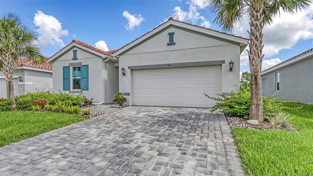 A single-story house with a paved driveway, two-car garage, and blue shutters under a blue sky — 491 DAYLILY BOULEVARD, NOKOMIS, FL