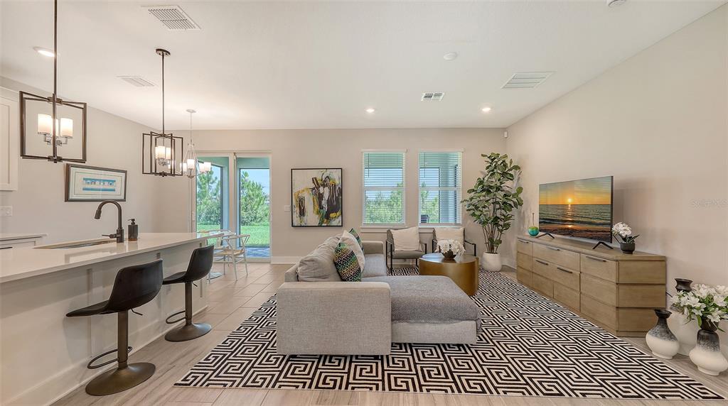 A modern open-concept living room features a kitchen island, gray sectional sofa, and television console — 491 DAYLILY BOULEVARD, NOKOMIS, FL