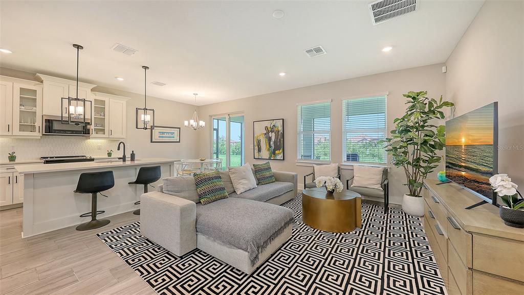 An open-concept living room and kitchen feature a sectional sofa, area rug, and island seating — 491 DAYLILY BOULEVARD, NOKOMIS, FL