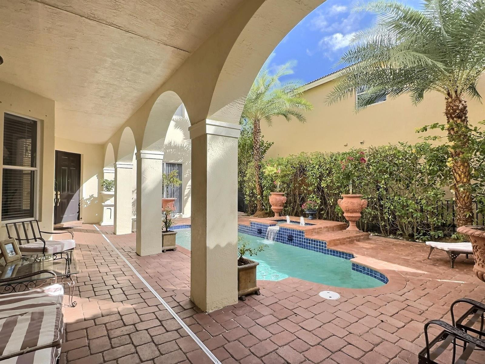 A covered patio with arched columns overlooks a small swimming pool and a landscaped courtyard — 9183 Nugent Trail, West Palm Beach FL 33411, WEST PALM BEACH, FL