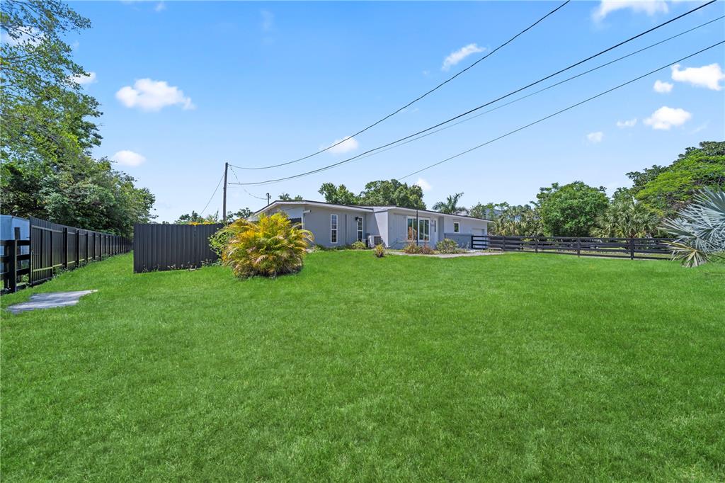 A grassy backyard features a single-story house, a black fence, and a large palm bush — 1507 LAVILLA ROAD, PUNTA GORDA, FL