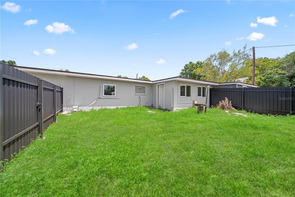 A grassy backyard features a gray house exterior with a black privacy fence — 1507 LAVILLA ROAD, PUNTA GORDA, FL