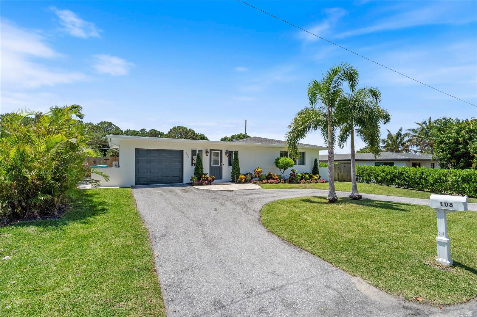 A single-story white house with a gray garage door and a curved asphalt driveway — 108 SE 31st Avenue, Boynton Beach FL 33435, BOYNTON BEACH, FL