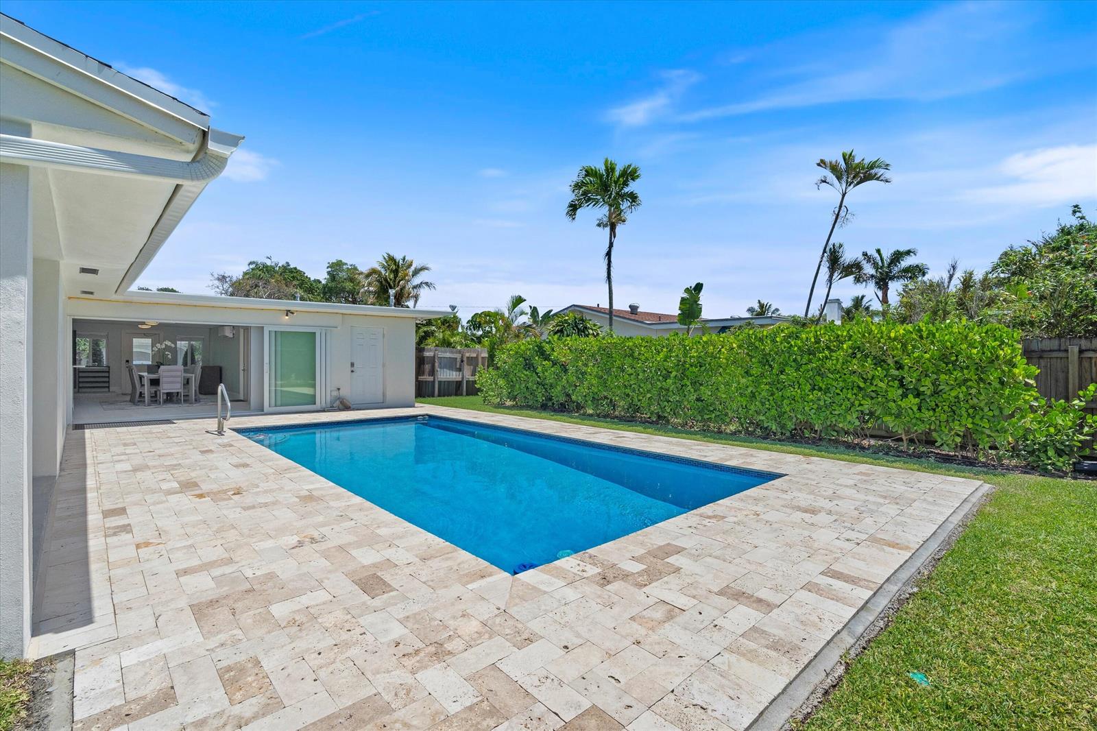 A rectangular swimming pool sits on a stone patio next to a house and hedge — 108 SE 31st Avenue, Boynton Beach FL 33435, BOYNTON BEACH, FL