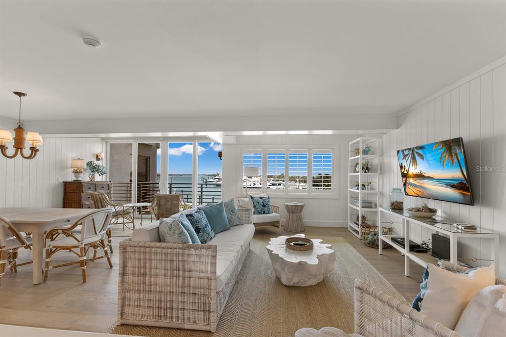 A bright living and dining room features coastal decor, white paneled walls, and a water view — 5850 GASPARILLA ROAD UNIT M1&3, BOCA GRANDE, FL