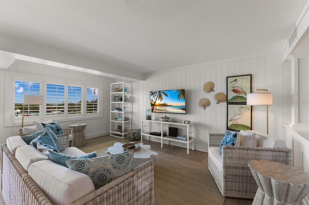 A coastal-style living room features white shiplap walls, wicker furniture, and a television above a console — 5850 GASPARILLA ROAD UNIT M1&3, BOCA GRANDE, FL