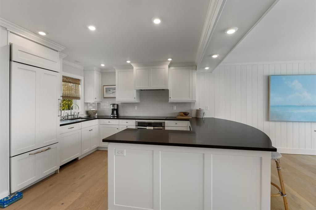 A white kitchen features dark countertops, light wood flooring, and a curved breakfast bar — 5850 GASPARILLA ROAD UNIT M1&3, BOCA GRANDE, FL