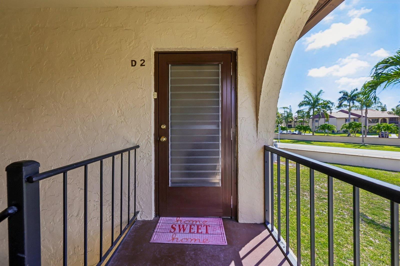 An exterior view of a brown front door labeled D2 with a welcome mat — 5773 La Paseos Drive # 2, FL 33463, FL