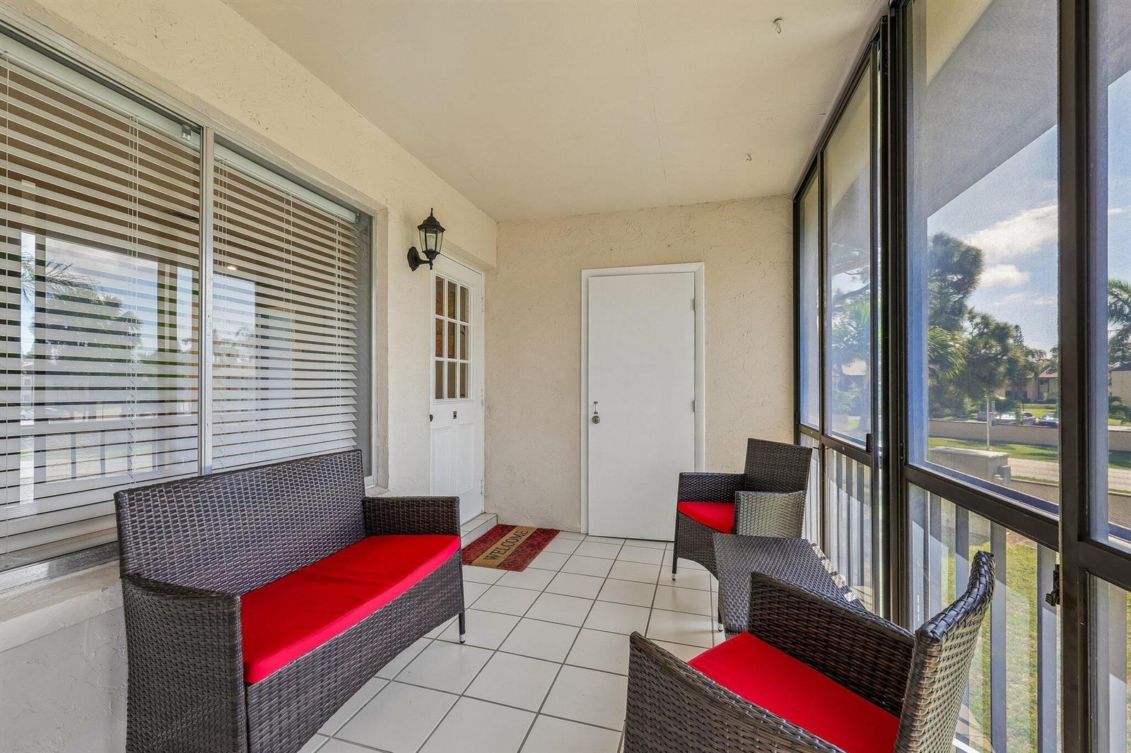 A screened-in porch features white tile flooring, wicker furniture with red cushions, and large windows — 5773 La Paseos Drive # 2, FL 33463, FL