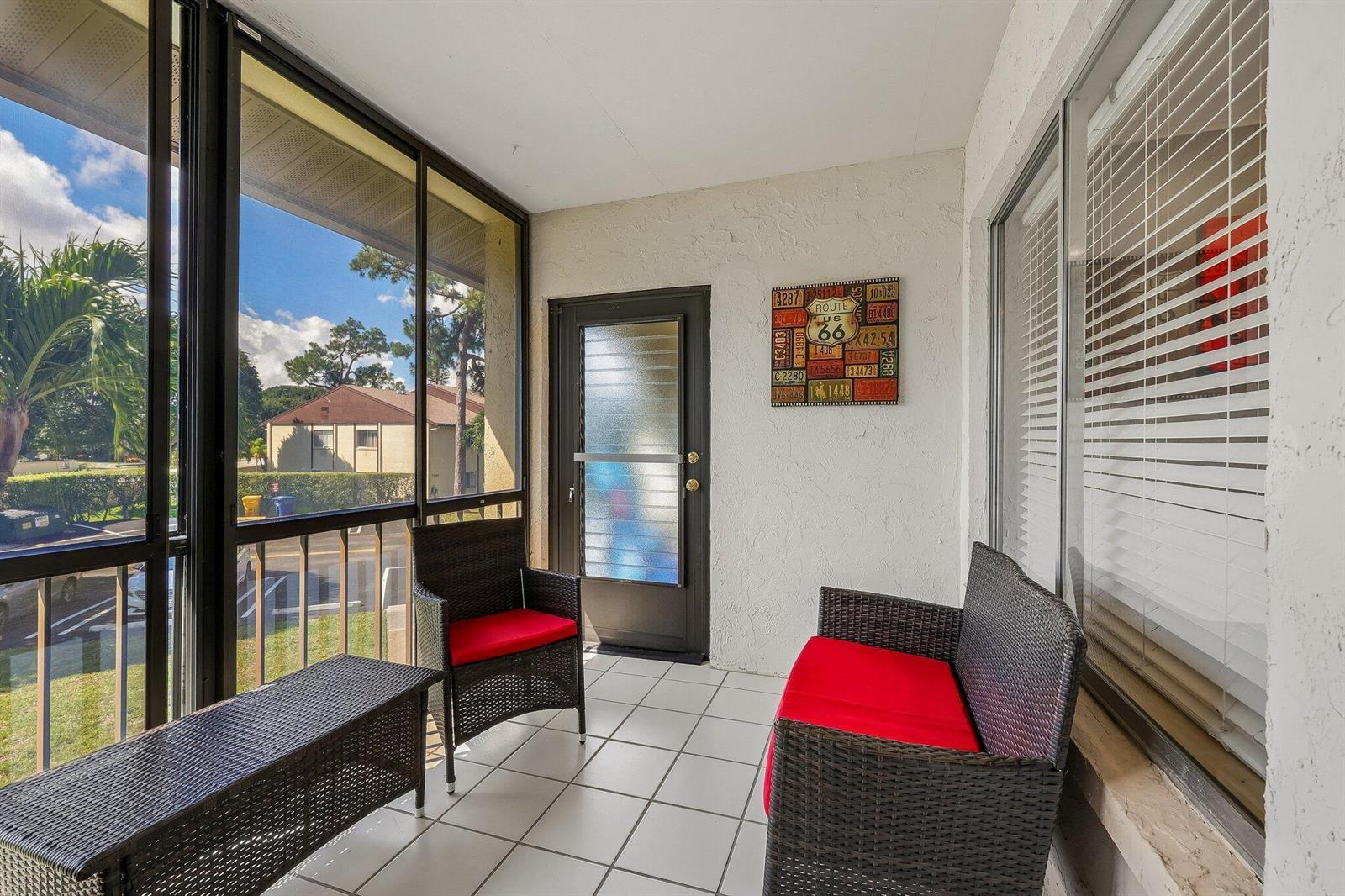 A screened-in porch features white tile flooring, wicker furniture with red cushions, and a door — 5773 La Paseos Drive # 2, FL 33463, FL