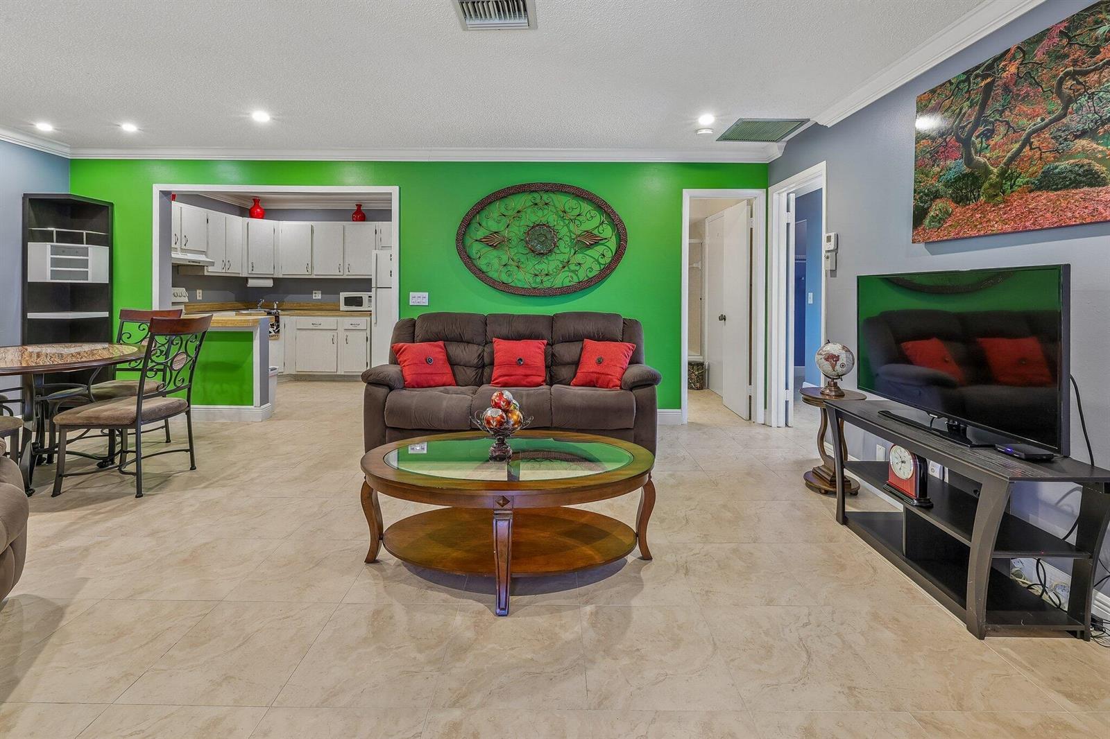 A living room with a green accent wall, brown sofa, glass coffee table, and tile flooring — 5773 La Paseos Drive # 2, FL 33463, FL