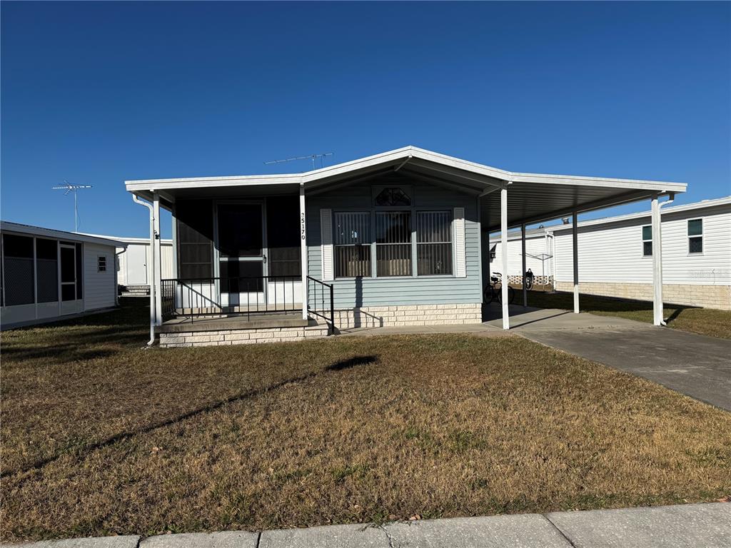 A light blue manufactured home features a front porch, a carport, and a brick-patterned base — 35170 DANNY DRIVE UNIT 159, ZEPHYRHILLS, FL