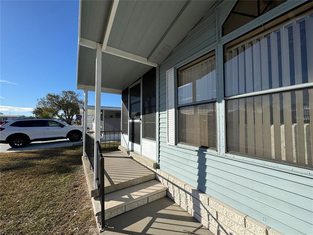 A light blue mobile home exterior features a covered concrete porch with black railings — 35170 DANNY DRIVE UNIT 159, ZEPHYRHILLS, FL