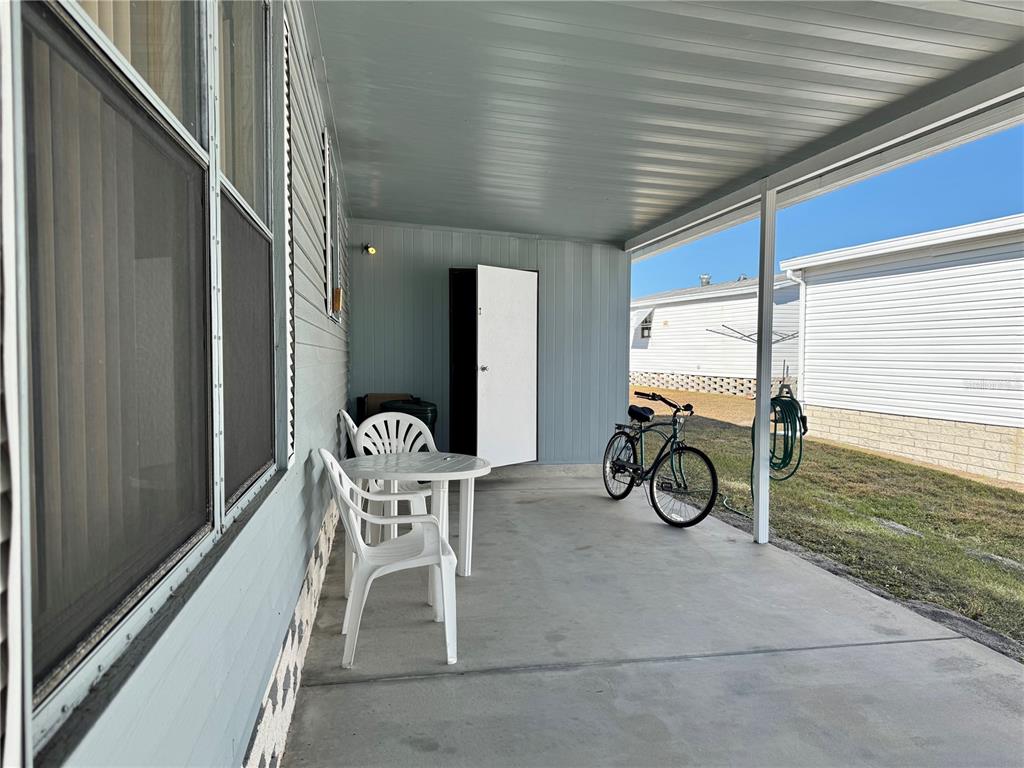 A covered concrete patio features a small table with two chairs, a bicycle, and storage — 35170 DANNY DRIVE UNIT 159, ZEPHYRHILLS, FL