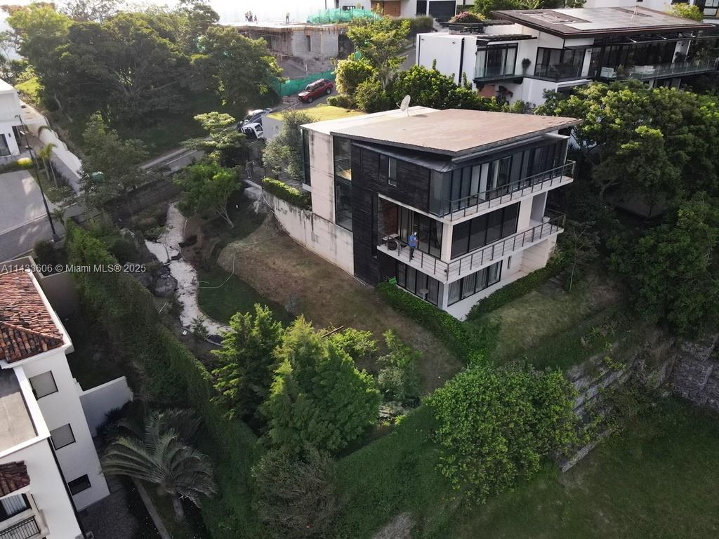 An aerial view shows a modern three-story house with dark siding and balconies on a hillside — 46 Cerro Real Alto Las Palomas, CR, CR