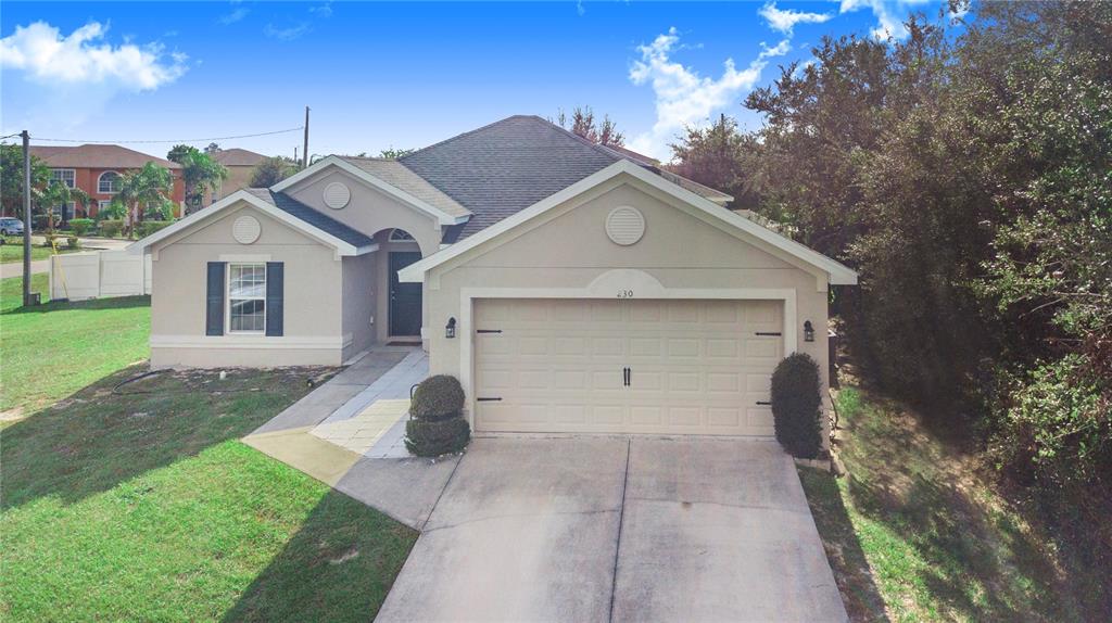 A single-story suburban house features a beige stucco exterior, a two-car garage, and a driveway — 230 GROUPER COURT, POINCIANA, FL