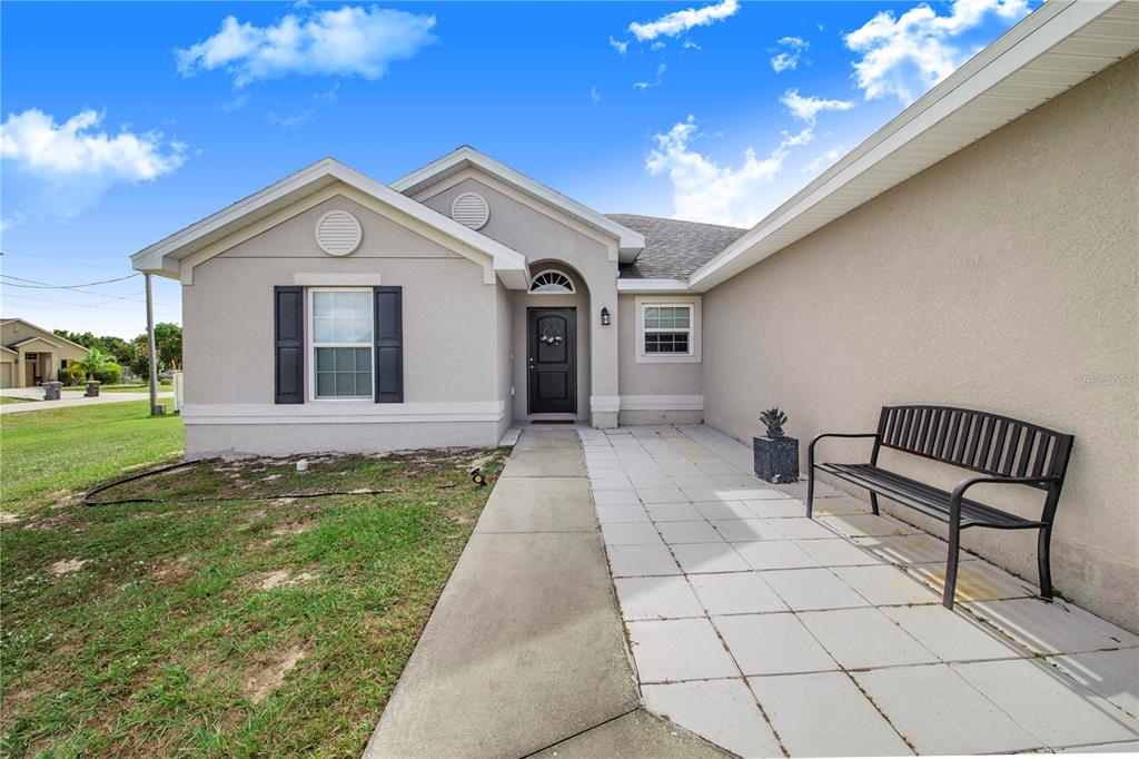 A light-colored house exterior features a front walkway, a black bench, and a dark door — 230 GROUPER COURT, POINCIANA, FL
