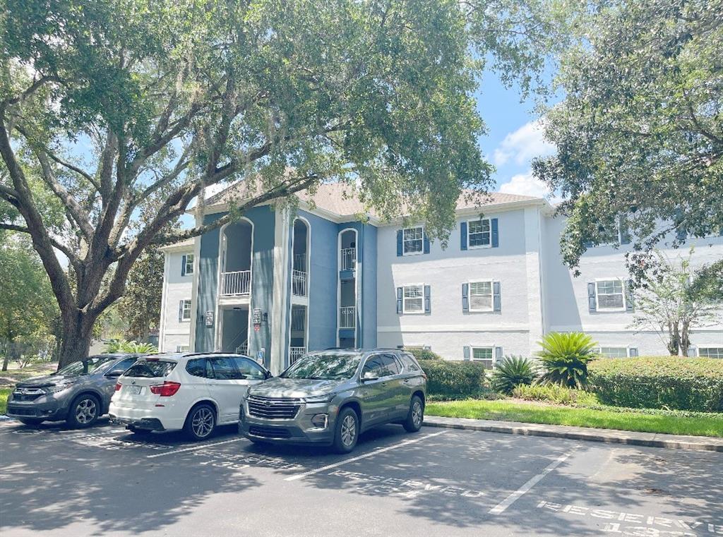 A three-story apartment building with blue accents and parked cars in front — 8203 OLYMPIA COURT UNIT 8203, LONGWOOD, FL