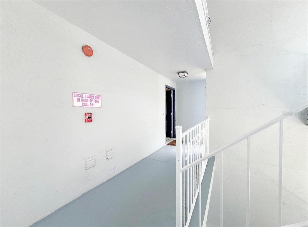 An outdoor apartment hallway features white walls, a gray floor, and a metal railing — 8203 OLYMPIA COURT UNIT 8203, LONGWOOD, FL