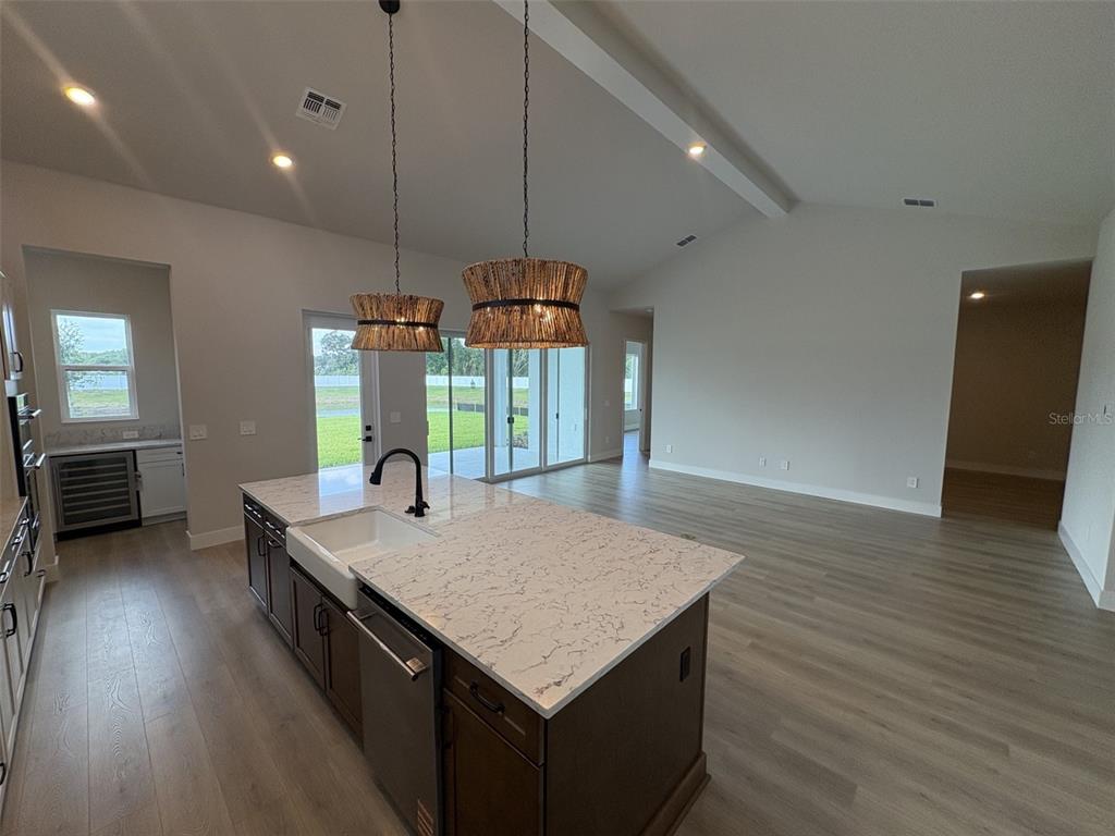 A modern kitchen features white cabinetry, a large marble-topped island, and two textured pendant lights — 7245 MEADOWSHADE COURT, SARASOTA, FL