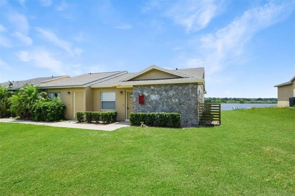 A single-story residential building with a stone facade sits on a grassy lawn near water — 1184 WOODMAN WAY, ORLANDO, FL