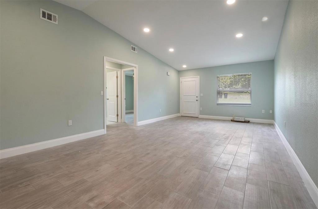 A spacious living room features light blue walls, recessed lighting, and wood-look tile flooring — 1184 WOODMAN WAY, ORLANDO, FL
