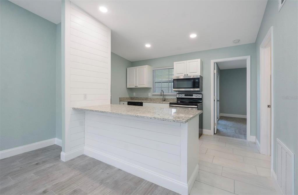 A kitchen features white shiplap cabinetry, granite countertops, and light blue walls — 1184 WOODMAN WAY, ORLANDO, FL