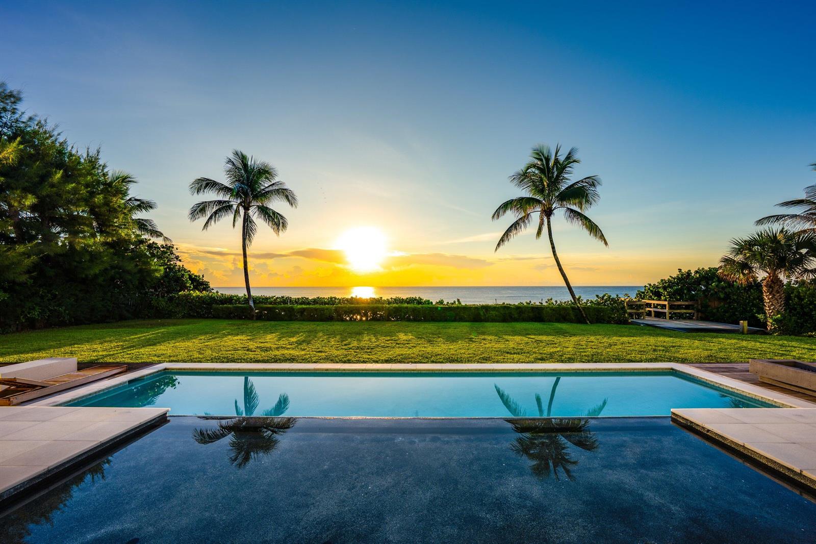 An infinity pool overlooks a grassy lawn, palm trees, and the ocean at sunset — 6273 N Ocean Boulevard, Ocean Ridge FL 33435, OCEAN RIDGE, FL