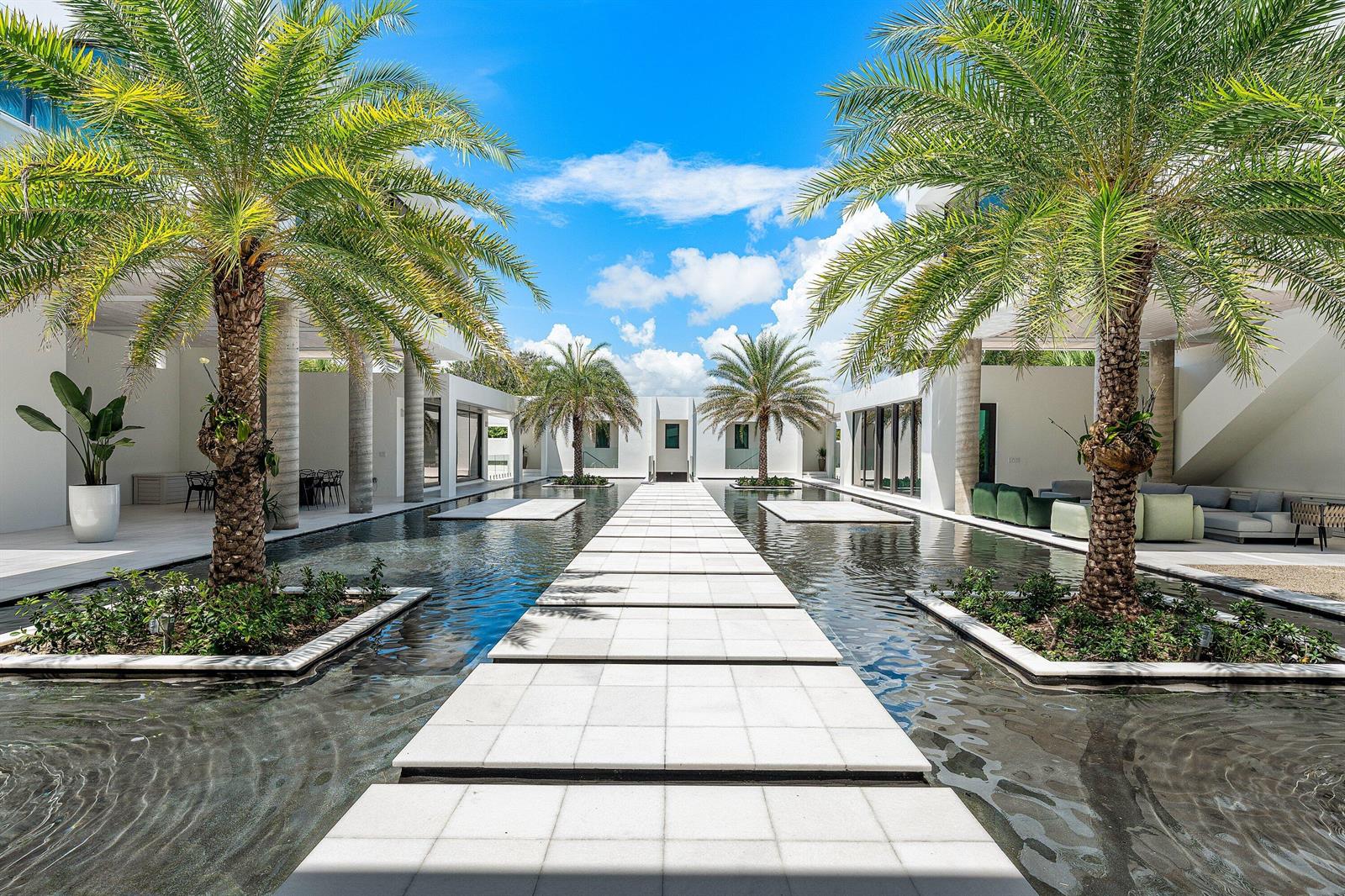 A modern courtyard features a central stone walkway surrounded by water, palm trees, and buildings — 6273 N Ocean Boulevard, Ocean Ridge FL 33435, OCEAN RIDGE, FL