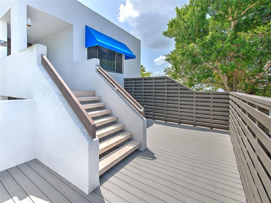An outdoor wooden deck features a staircase leading to a white building with blue awnings — 519 BAYPORT WAY UNIT 519, LONGBOAT KEY, FL