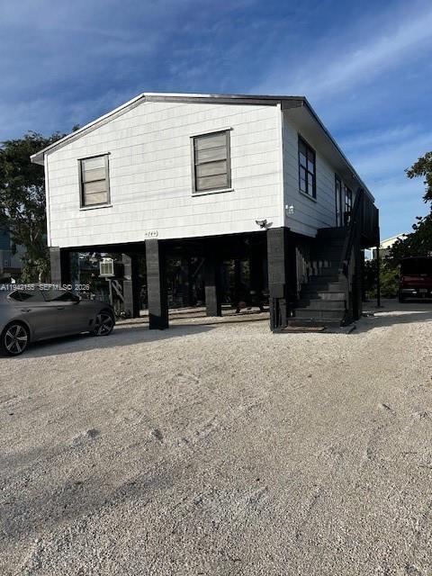 An elevated white house with black support pillars stands above a gravel driveway — 74 Pelican Ln, Big Pine FL 33043, BIG PINE, FL