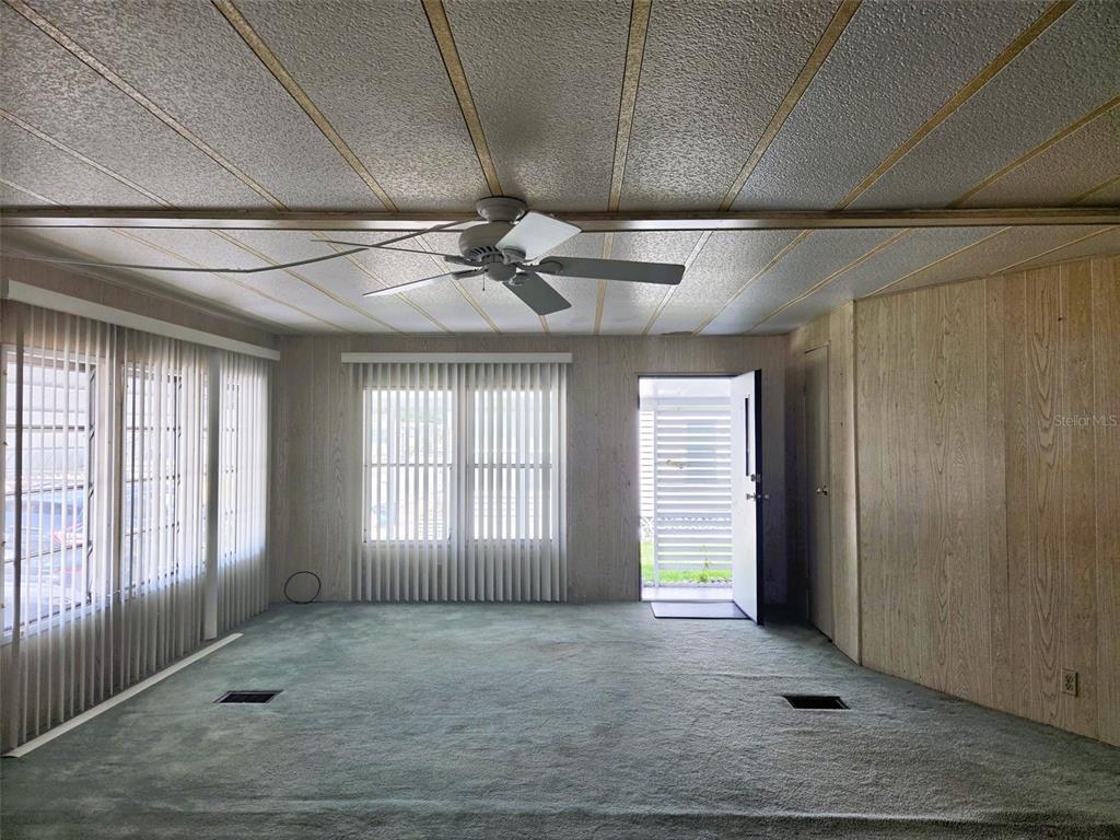 A living room features wood-paneled walls, green carpeting, a ceiling fan, and vertical window blinds — 3329 OAKWOOD BOULEVARD S, SARASOTA, FL