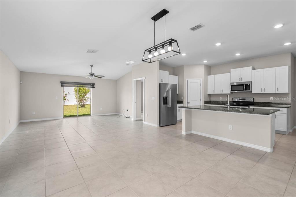 An open-concept kitchen and living area with tile flooring, stainless steel appliances, and sliding doors — 6823 KING CREEK DRIVE, SUN CITY CENTER, FL