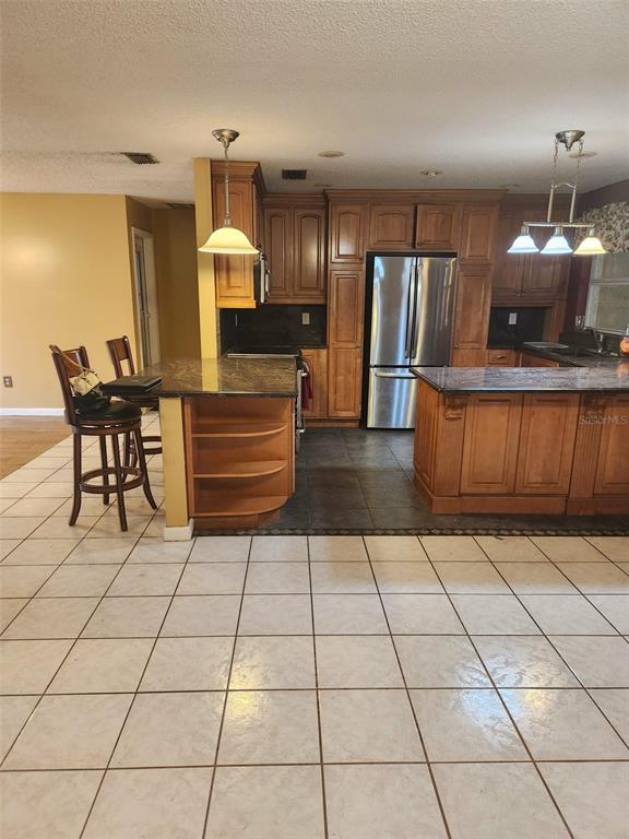 A kitchen features wood cabinets, dark granite countertops, stainless steel appliances, and white tile flooring — 3215 LAKE SAXON DRIVE, LAND O LAKES, FL