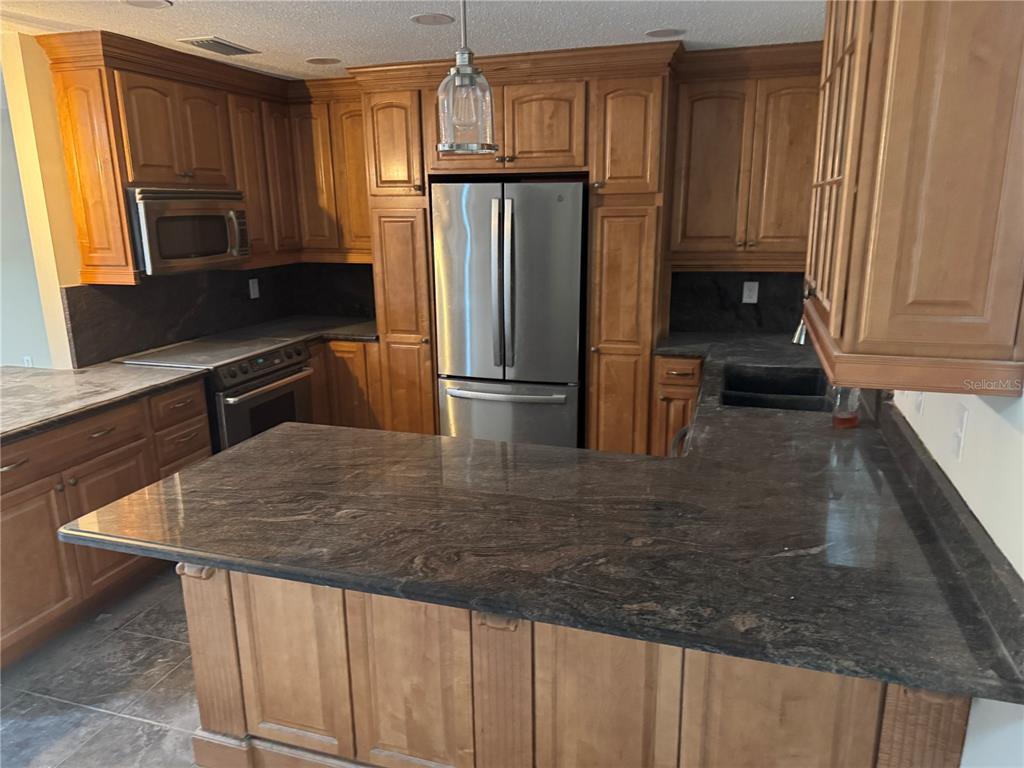 A kitchen features wood cabinetry, dark granite countertops, and stainless steel appliances — 3215 LAKE SAXON DRIVE, LAND O LAKES, FL