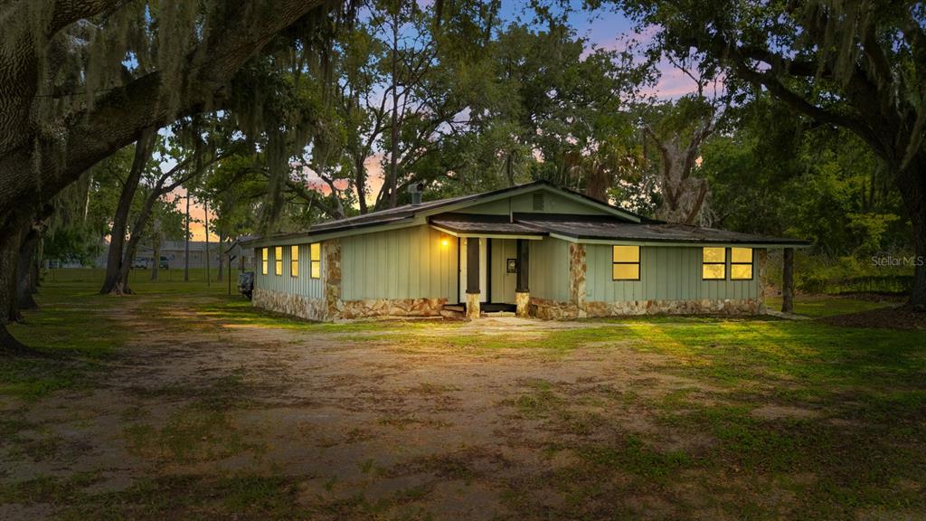 A single-story house with green vertical siding, stone accents, and a stone walkway — 12616 THONOTOSASSA ROAD, THONOTOSASSA, FL