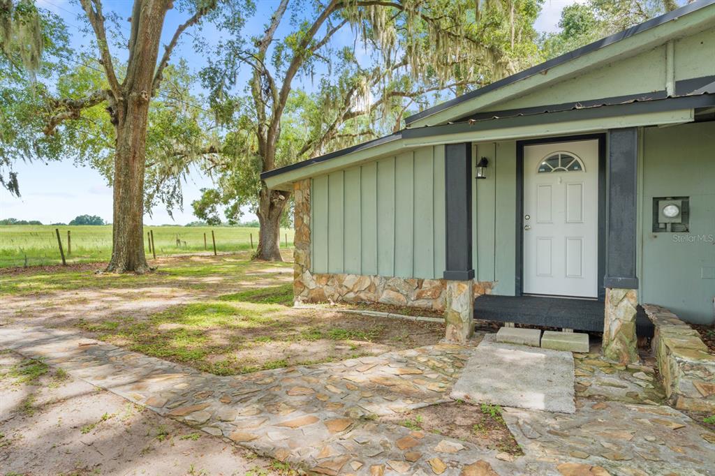 A single-story house with light green vertical siding and stone accents sits among trees — 12616 THONOTOSASSA ROAD, THONOTOSASSA, FL