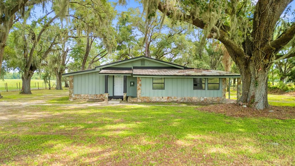 A green house with stone accents and a white front door sits near large trees — 12616 THONOTOSASSA ROAD, THONOTOSASSA, FL