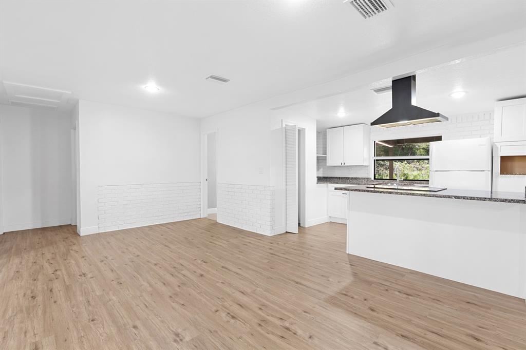 A bright kitchen and dining area feature white cabinets, a breakfast bar, and wood flooring — 12616 THONOTOSASSA ROAD, THONOTOSASSA, FL