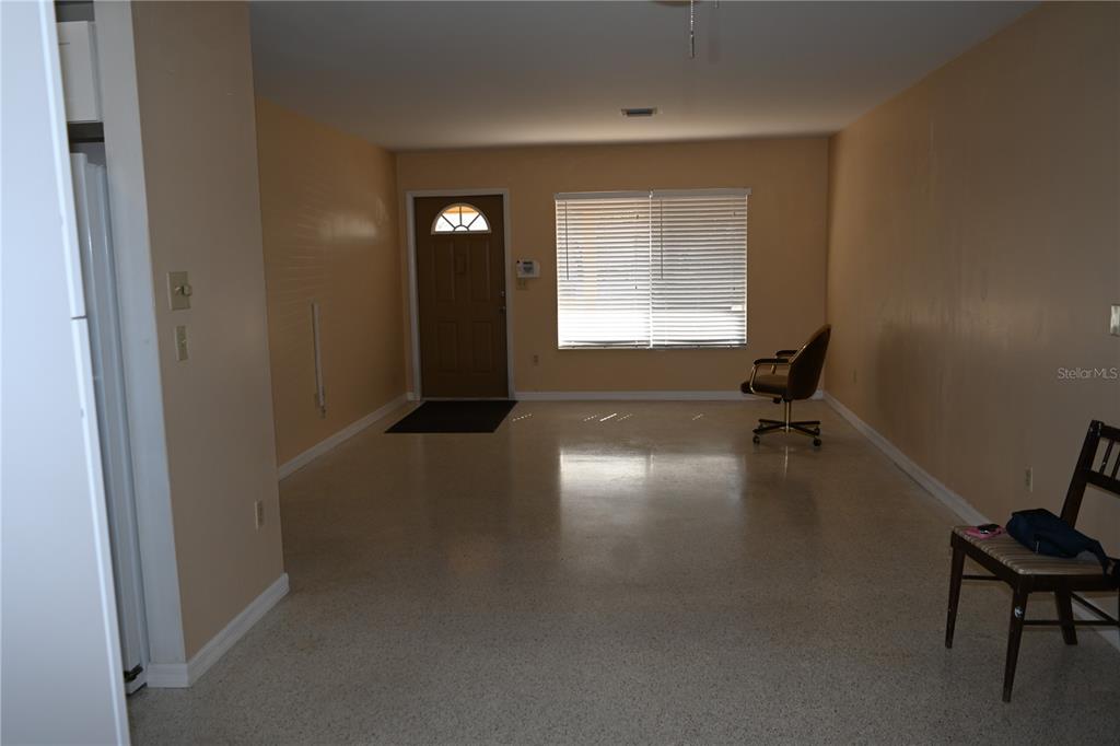 An empty room with tan walls, a front door, a window with blinds, and terrazzo flooring — 8298 FAY AVENUE, NORTH PORT, FL