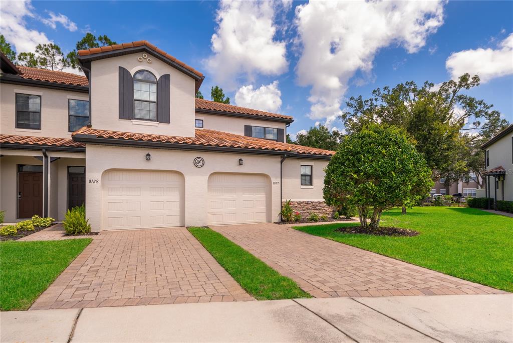 A two-story townhouse features a beige stucco exterior, two garage doors, and a paved driveway — 8127 ROSEVILLE BOULEVARD, DAVENPORT, FL