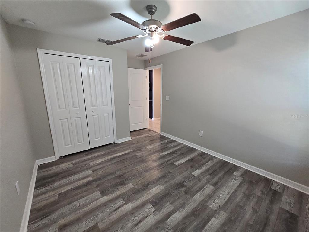 A bedroom with gray walls, wood-look flooring, a ceiling fan, and white closet doors — 838 OLIVE CONCH STREET, RUSKIN, FL