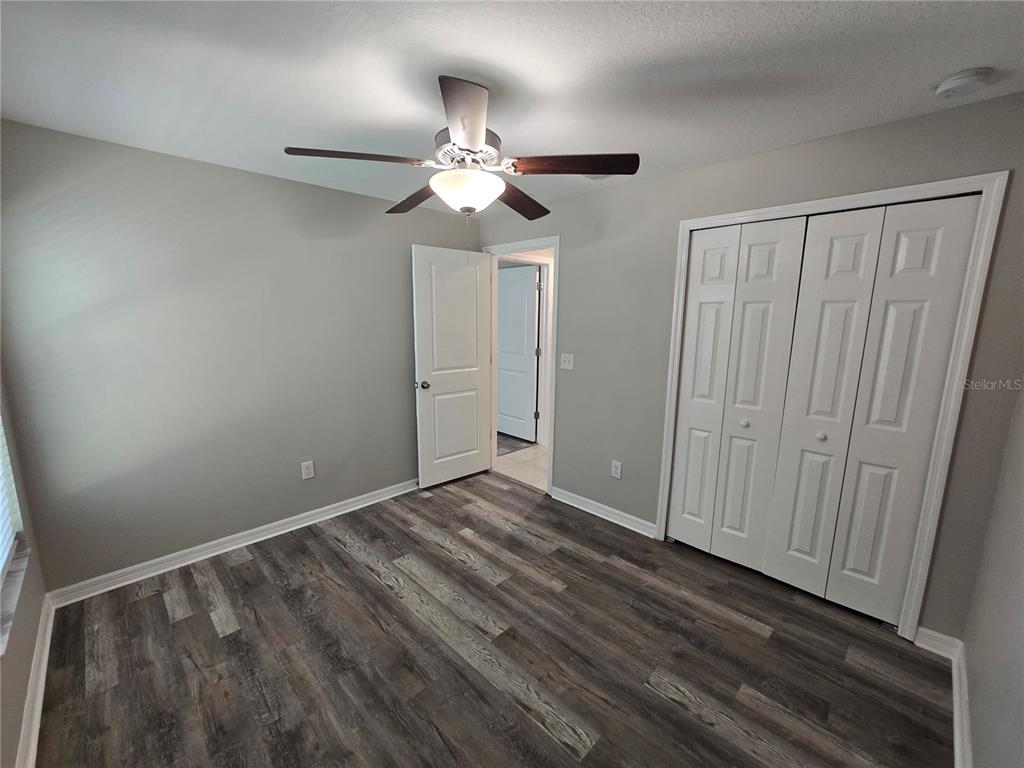 An empty bedroom features gray walls, wood-look flooring, a ceiling fan, and white closet doors — 838 OLIVE CONCH STREET, RUSKIN, FL