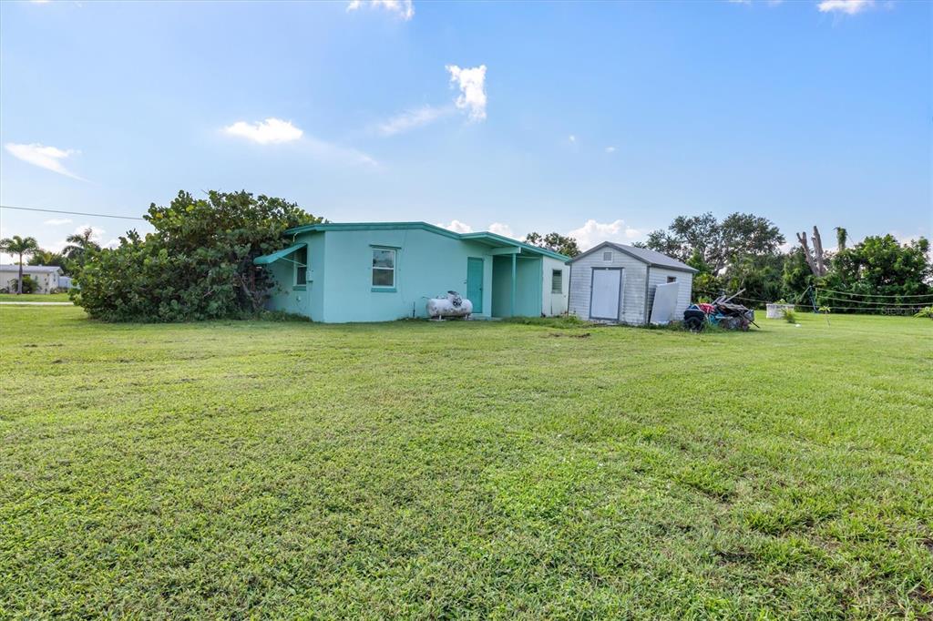 A light green single-story house stands on a large grassy lot with a small shed — 3107 EASY STREET, PORT CHARLOTTE, FL