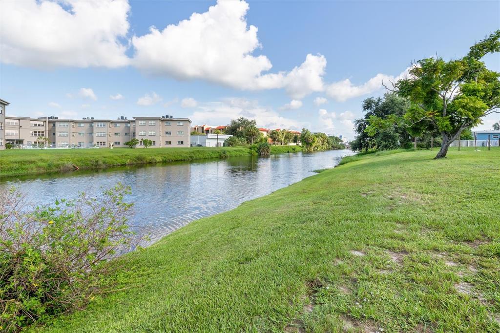 A grassy bank slopes down to a canal with apartment buildings in the background — 3107 EASY STREET, PORT CHARLOTTE, FL
