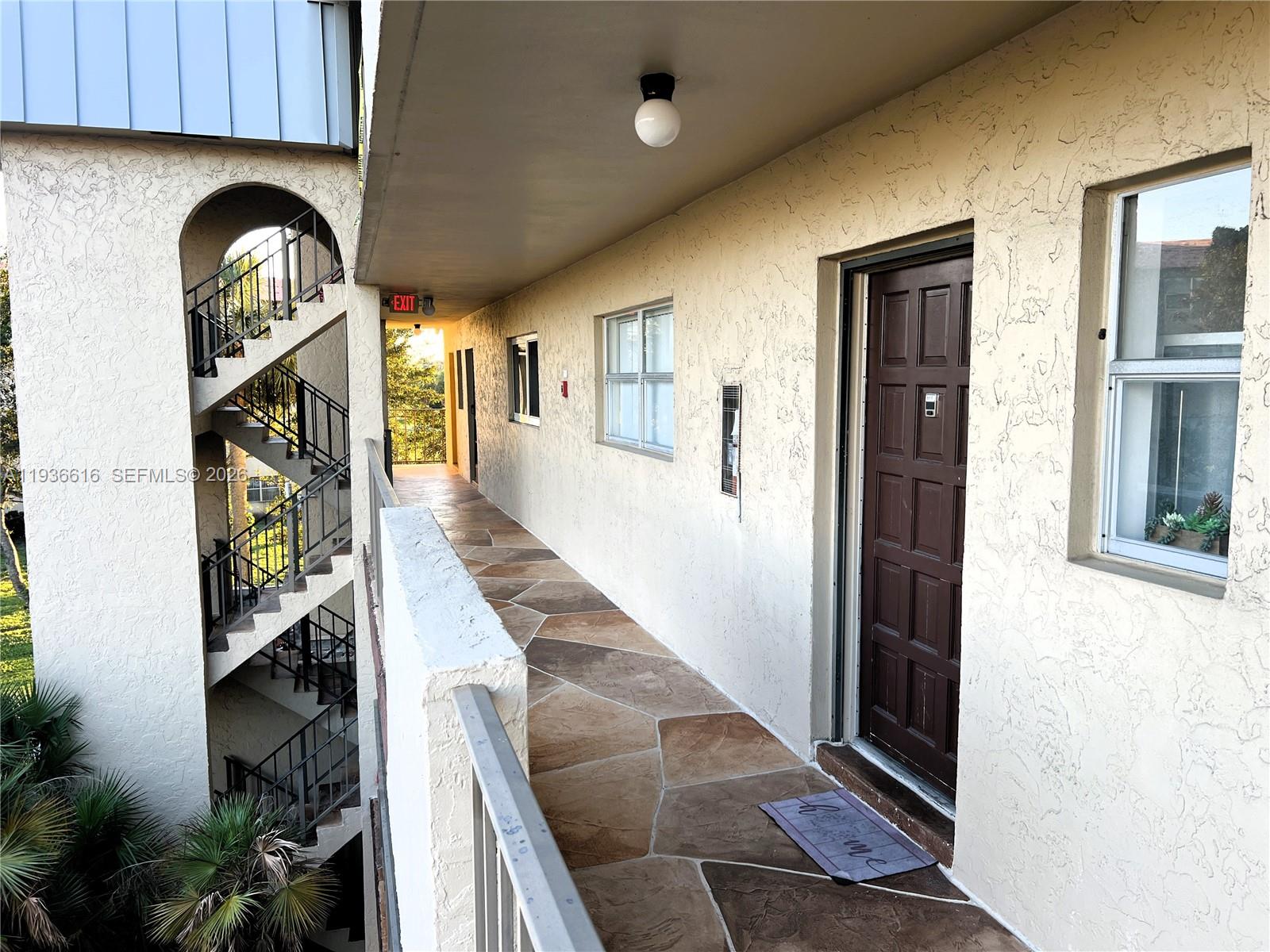 An exterior walkway with stone-patterned flooring leads to a brown door beside a window — 6301 N Falls Cir Dr # 313, Lauderhill FL 33319, LAUDERHILL, FL