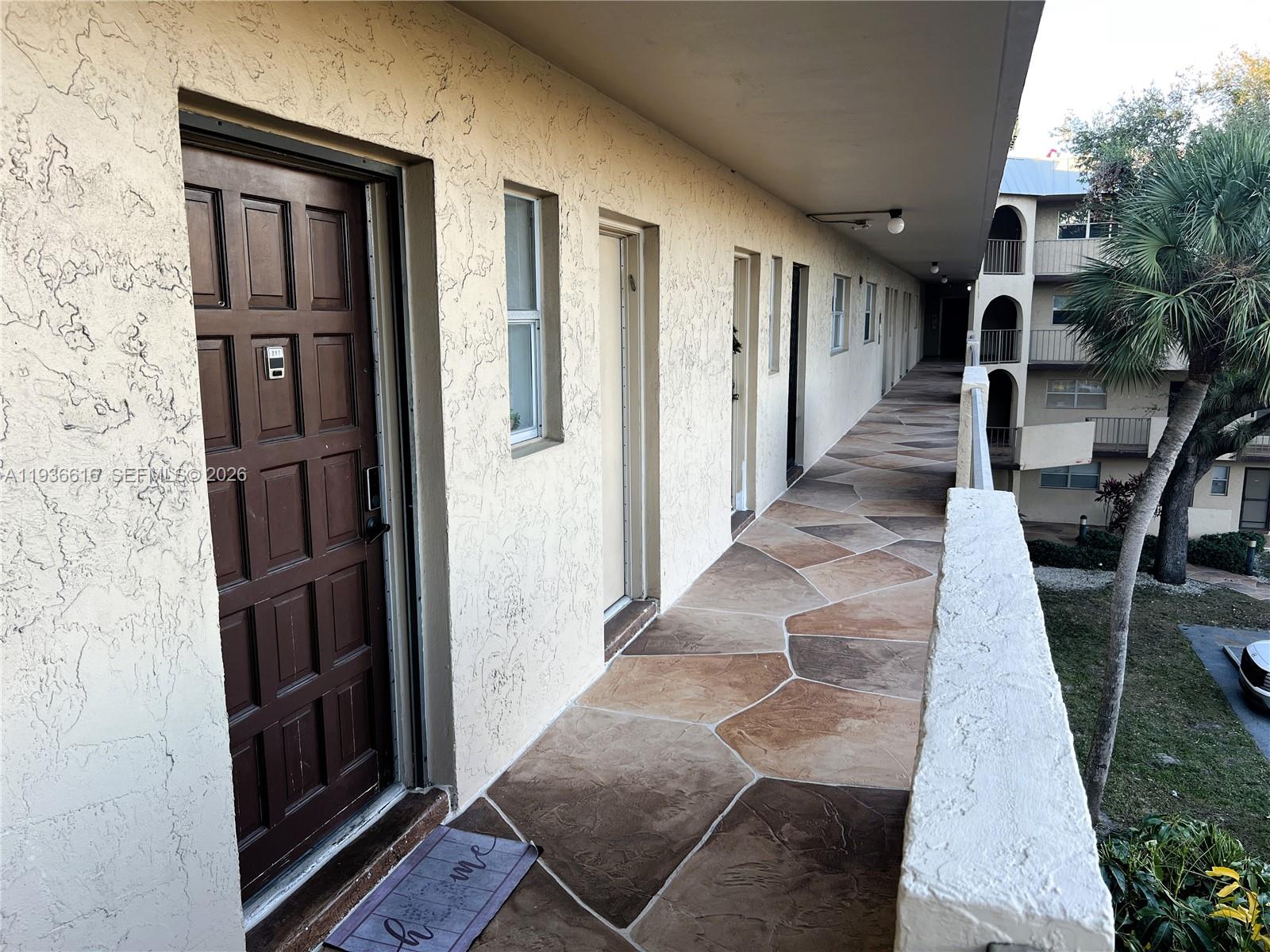 An exterior walkway with stone-patterned flooring leads past several apartment doors in a multi-story building — 6301 N Falls Cir Dr # 313, Lauderhill FL 33319, LAUDERHILL, FL