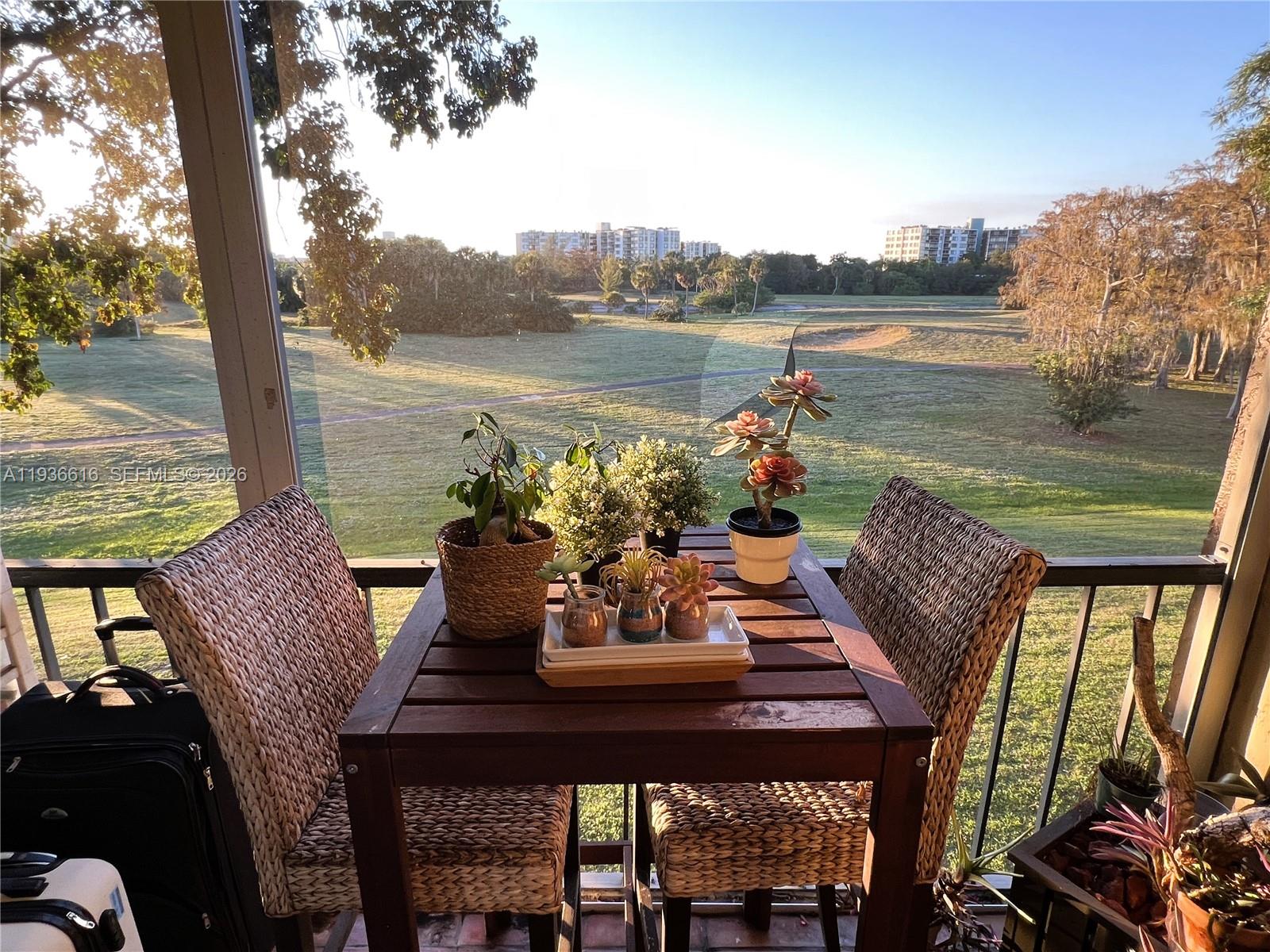 A balcony features a wooden table with potted plants and two wicker chairs overlooking a golf course — 6301 N Falls Cir Dr # 313, Lauderhill FL 33319, LAUDERHILL, FL