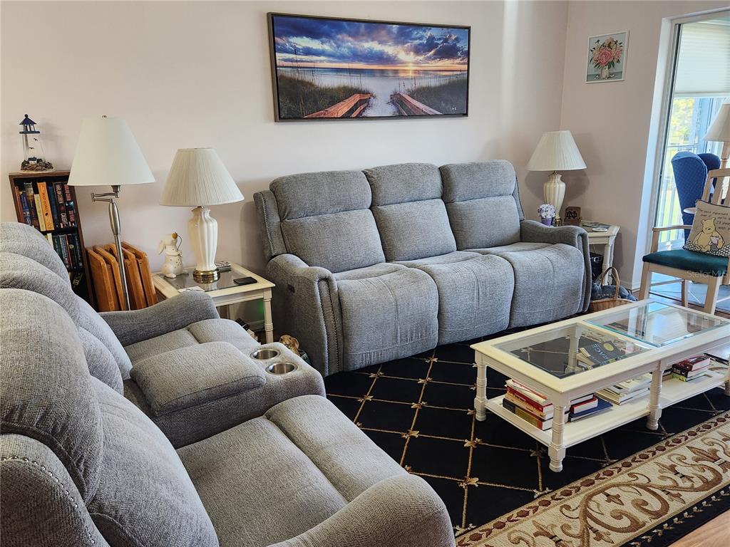 A living room features gray reclining sofas, a glass-topped coffee table, and a black rug — 6505 STONE RIVER ROAD UNIT 304, BRADENTON, FL