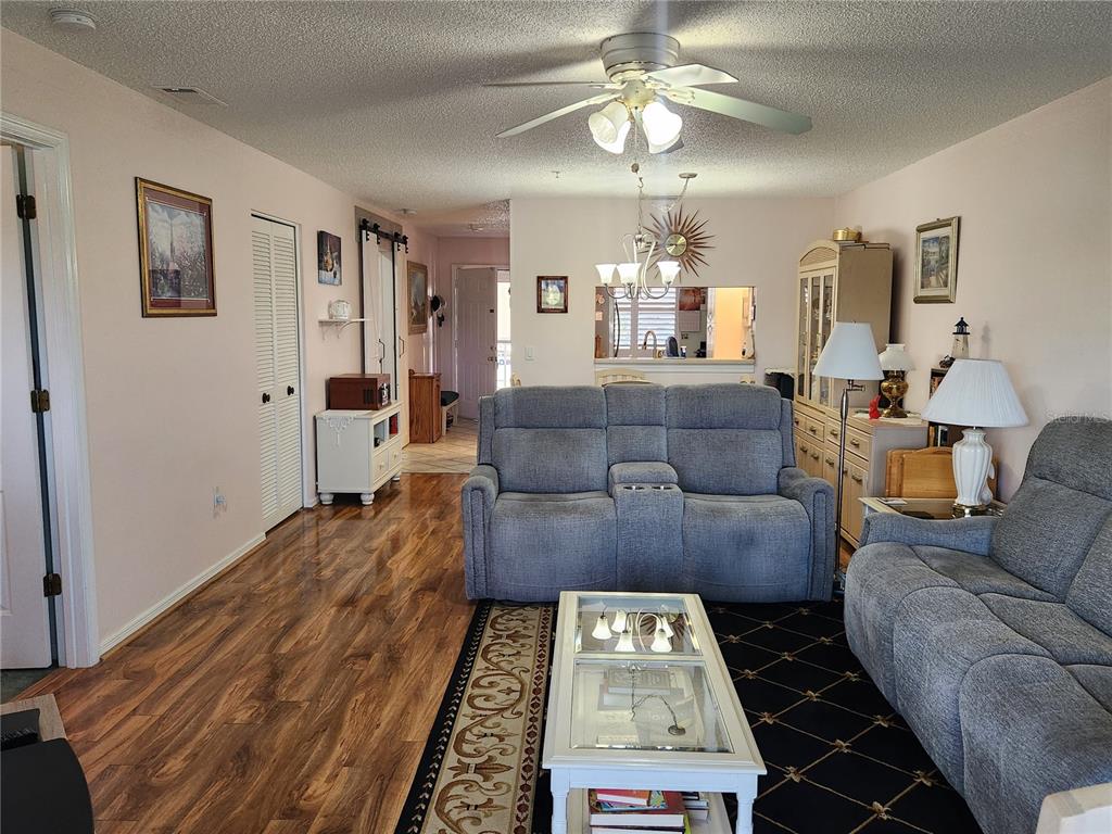 A living room features wood-look flooring, a gray reclining sofa, and a glass-topped coffee table — 6505 STONE RIVER ROAD UNIT 304, BRADENTON, FL